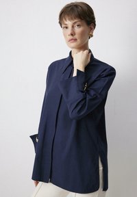 Navy blue button-up shirt made of lightweight fabric, featuring a collar, side slits, and decorative gold accents on the sleeves.