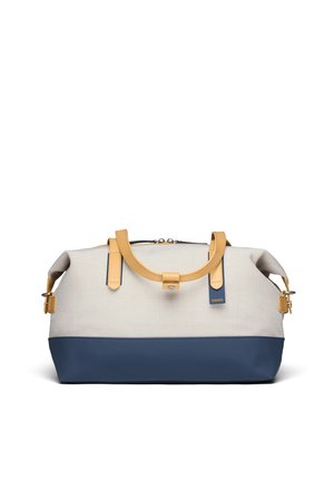 Zachte beige en marineblauwe weekendt tas met bruine leren handvatten en een klein etiket aan de voorkant in het midden, tegen een witte achtergrond.