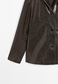 Bruine vinyljas met een ingesneden kraag, drie knopen en lange mouwen. Glad textuur met een licht glanzende afwerking.