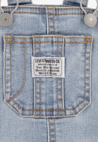 Ljusblå denimoverall har kopparstickning, en rektangulär bakficka och en etikett med "Levi Strauss & Co." på baksidan.