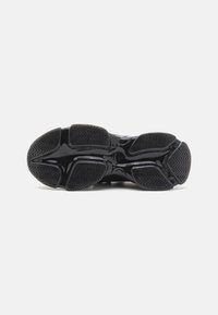 Black athletic shoe sole featuring a textured rubber surface with zigzag patterns and a glossy finish, designed for traction and durability.