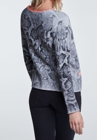 Pull léger gris avec un motif serpent. Il présente un col rond avec une bordure rose et des manches longues. Porté avec un jean noir.