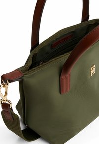 Olivgrüne Nylon-Tasche mit braunen Lederrändern und einem goldenen Logo. Verfügt über einen oberen Reißverschluss und einen abnehmbaren Schulterriemen.
