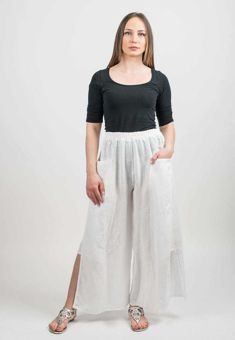 Un haut noir à manches longues associé à un pantalon en lin blanc, ample, avec des poches latérales et des fentes, complété par des sandales décoratives.