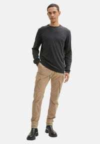 Dunkelgrauer langärmeliger Pullover kombiniert mit beigen Cargohosen mit seitlichen Taschen, getragen mit schwarzen Stiefeletten. Einfaches, lässiges Outfit.