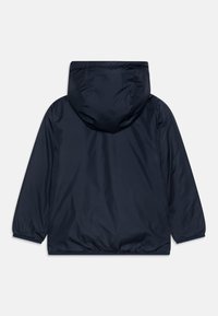 Giacca impermeabile blu navy con cappuccio, polsini elasticizzati e orlo arricciato. Texture liscia con design minimalista e senza hardware visibile.