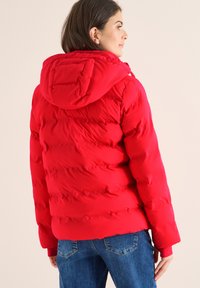 Rote Pufferjacke mit Kapuze, ausgestattet mit einem gesteppte Design und elastischen Bündchen. Der Stoff wirkt glatt mit einem leichten Glanz und eignet sich für kaltes Wetter.