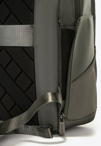 Sac à dos en tissu gris foncé avec un panneau texturé noir, des accents argentés, une poche zippée et un design de sangle tissée plate.