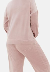 Set di abbigliamento loungewear rosa a coste composto da una maglietta a maniche lunghe e pantaloni con vita elastica dotati di una piccola tasca posteriore, realizzato in un tessuto morbido.