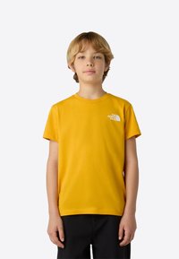 Camiseta amarilla de manga corta, hecha de algodón, con un pequeño logo blanco en el área izquierda del pecho. Diseño sencillo con cuello redondo.