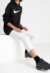 Svart hoodie med vitt Nike-logotyp, ljusblå uppvikta jeans och svarta luftsula sneakers. Slät tygkvalitet och avslappnad passform.