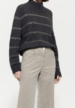Donkergrijze gebreide trui met horizontale metallic strepen gecombineerd met lichtbeige hoge taille broek met voorzakken.