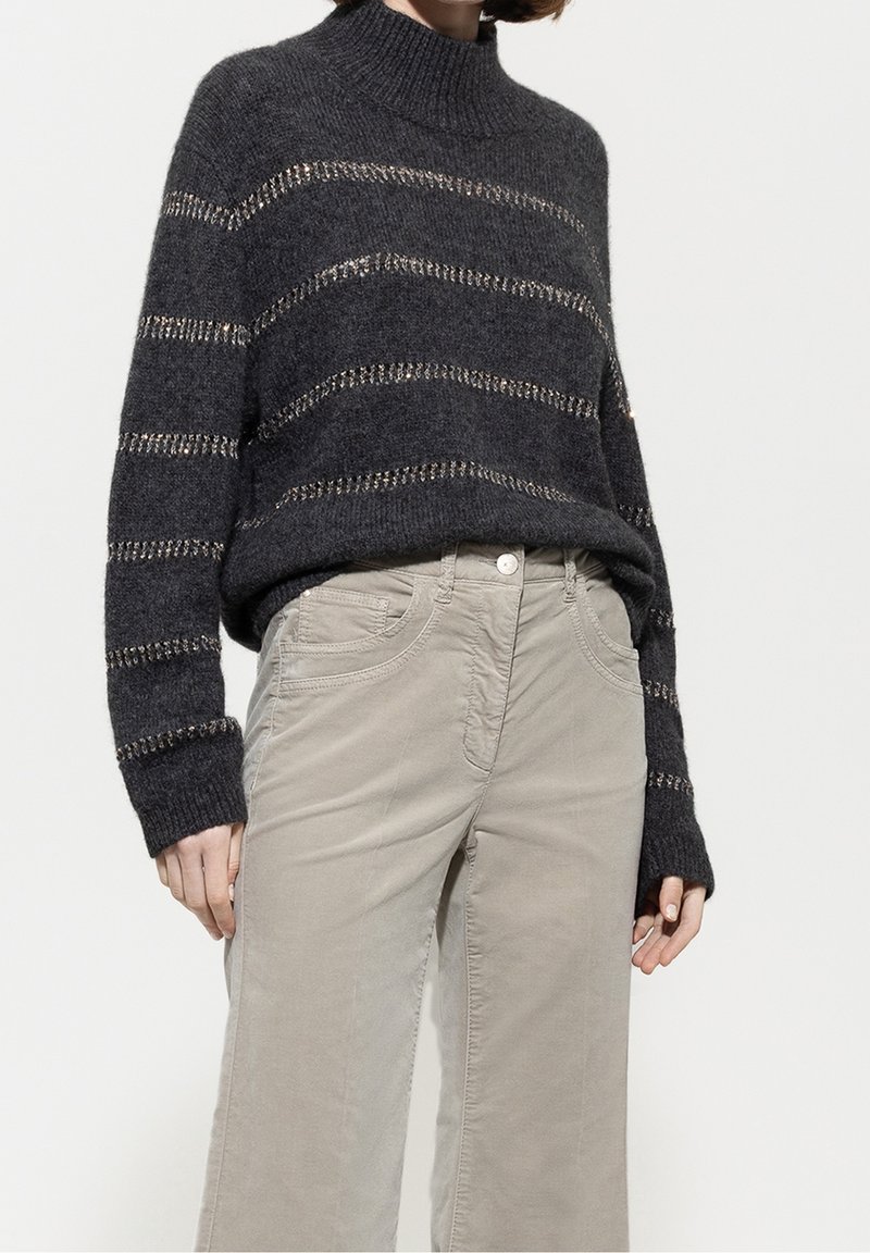 Pull en maille gris foncé avec des rayures métalliques horizontales associé à un pantalon beige clair taille haute avec poches avant.