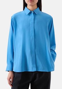 Camicia a maniche lunghe blu chiaro con colletto a punta, realizzata in tessuto liscio. Presenta una chiusura con bottoni e una vestibilità comoda.