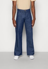 Blå denimbyxor med avslappnad passform, raka ben och stora framfickor. Avslutade med knappstängning och sömlös fåll.