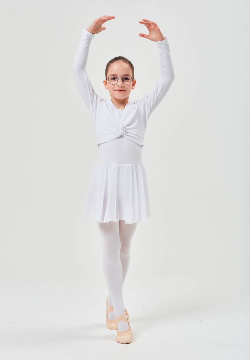 Weißes Langarm-Tanzoutfit mit Knotendetail, gestuftem Rock, weißen Strumpfhosen und rosa Ballettschuhen. Das Model trägt eine Brille und posiert in einer Ballettpose.