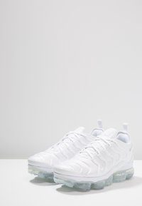 White athletic shoes with a textured, seamless upper. Clear, cushioned sole with prominent air bubbles. Laces threaded through a flexible design.