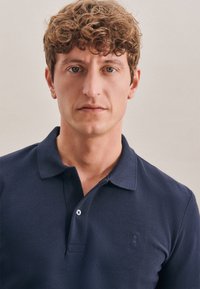 Granatowa koszulka polo wykonana z teksturowanej tkaniny; posiada klasyczny kołnierz, plisę na trzy guziki oraz małe haftowane logo na piersi.