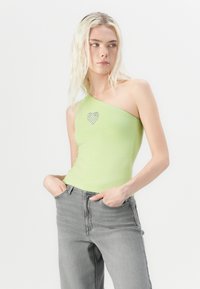Top verde chiaro a spalla unica in tessuto morbido con dettaglio di cuore in strass. Abbinato a jeans in denim grigio chiaro. Texture liscia.