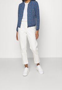 Blå bomberjakke med blomsterprint, hvid T-shirt, cremebukser og hvide sneakers. Glat tekstur, tætsiddende design og afslappet stil.