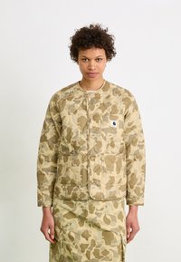 Tan camo quilted jacket with snap closures, round neck, and two front pockets. Features matching camo skirt with similar patterns.