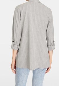 Blazer gris à fines rayures avec manches trois-quarts, poignets boutonnés et coupe cintrée. Texture lisse, tissu léger.