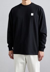 Sort langærmet t-shirt lavet af bomuld med en hvid logo på venstre bryst. Simpelt design med rund halsudskæring og afslappet pasform.