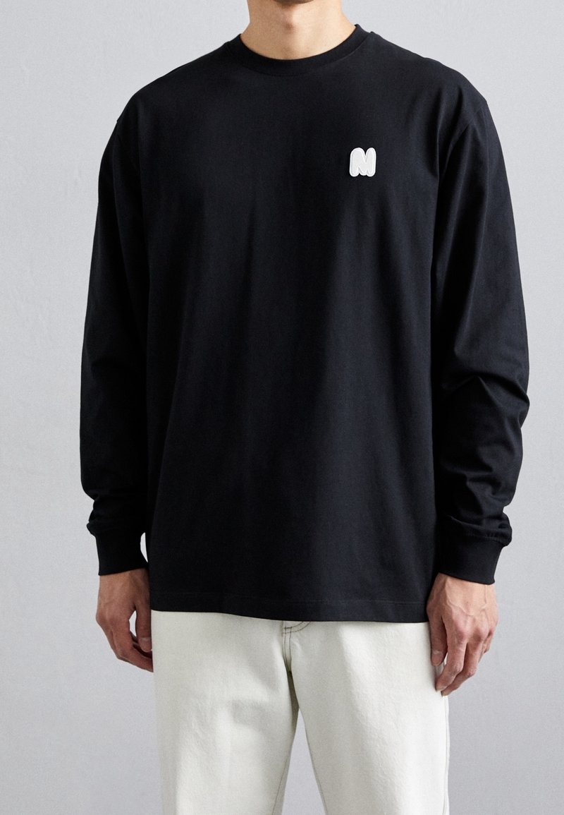 Sort langærmet t-shirt lavet af bomuld med en hvid logo på venstre bryst. Simpelt design med rund halsudskæring og afslappet pasform.