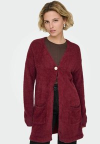 Burgundia karvane kardigan avatud ees, kahe eesmise tasku ja dekoratiivse nööbiga. Omab pikki varrukaid ja tekstureeritud kangast.