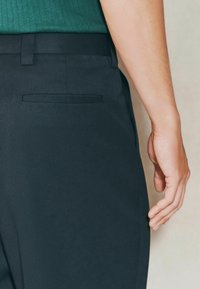 Tamne hlače s glatkom teksturom, s bočnom džepom i krojem koji se dobro uklapa. Pasica je ravna, što upotpunjuje elegantan dizajn.