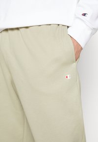 Ljusgröna sweatpants i mjukt material, med sidofickor och en liten logotyp i rött och blått på vänster lår.