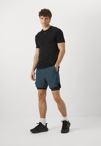 Camiseta atlética negra de manga corta combinada con pantalones cortos de color teal y zapatillas negras. La tela parece ligera y suave, con bolsillos laterales.