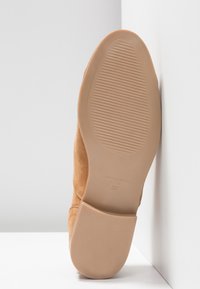 Bottine en daim beige avec un bout arrondi et une semelle en caoutchouc beige lisse. Présente des coutures discrètes et un logo sur la semelle. Taille 37.