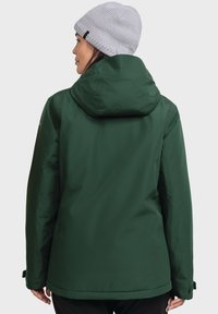 Grüne wasserfeste Jacke mit Kapuze, ausgestattet mit einer glatten Textur und verstellbaren Bündchen, getragen mit einer hellgrauen gestrickten Mütze.