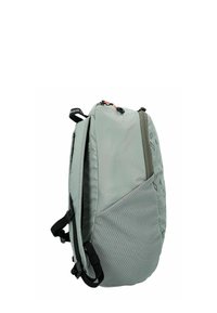 Mochila de color gris claro con superficie texturizada, que presenta un diseño elegante, múltiples cremalleras y correas ajustables. Acentos de color en verde oscuro.