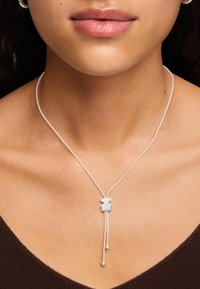 Srebrny naszyjnik z wisiorkiem w kształcie niedźwiedzia, z eleganckim łańcuszkiem i dwoma małymi zawieszkami. Gładka, lustrzana powierzchnia; minimalistyczny design.