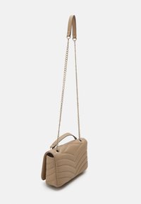 Beige gesteppte Handtasche mit Kettenriemen und einem oberen Tragegriff, ausgestattet mit einer glatten Textur und einem geschwungenen Wellenmuster.