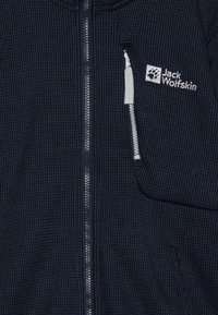Veste en polaire navy avec un motif texturé, fermeture éclair centrale et une poche zippée sur le côté gauche de la poitrine comportant le logo Jack Wolfskin.