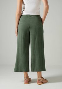 Gröna, vida linbyxor med resårmidja och sidofickor. Kombinerade med platta, remmade sandaler.