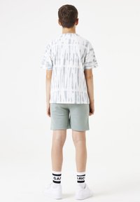 Camiseta de manga corta en tie-dye blanco y gris, combinada con pantalones cortos de color verde claro. Zapatillas blancas con calcetines de rayas en blanco y negro.