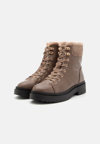 Bottines marron avec une tige en cuir lisse, doublure en fausse fourrure, œillets en métal doré et semelle en caoutchouc noir texturé.