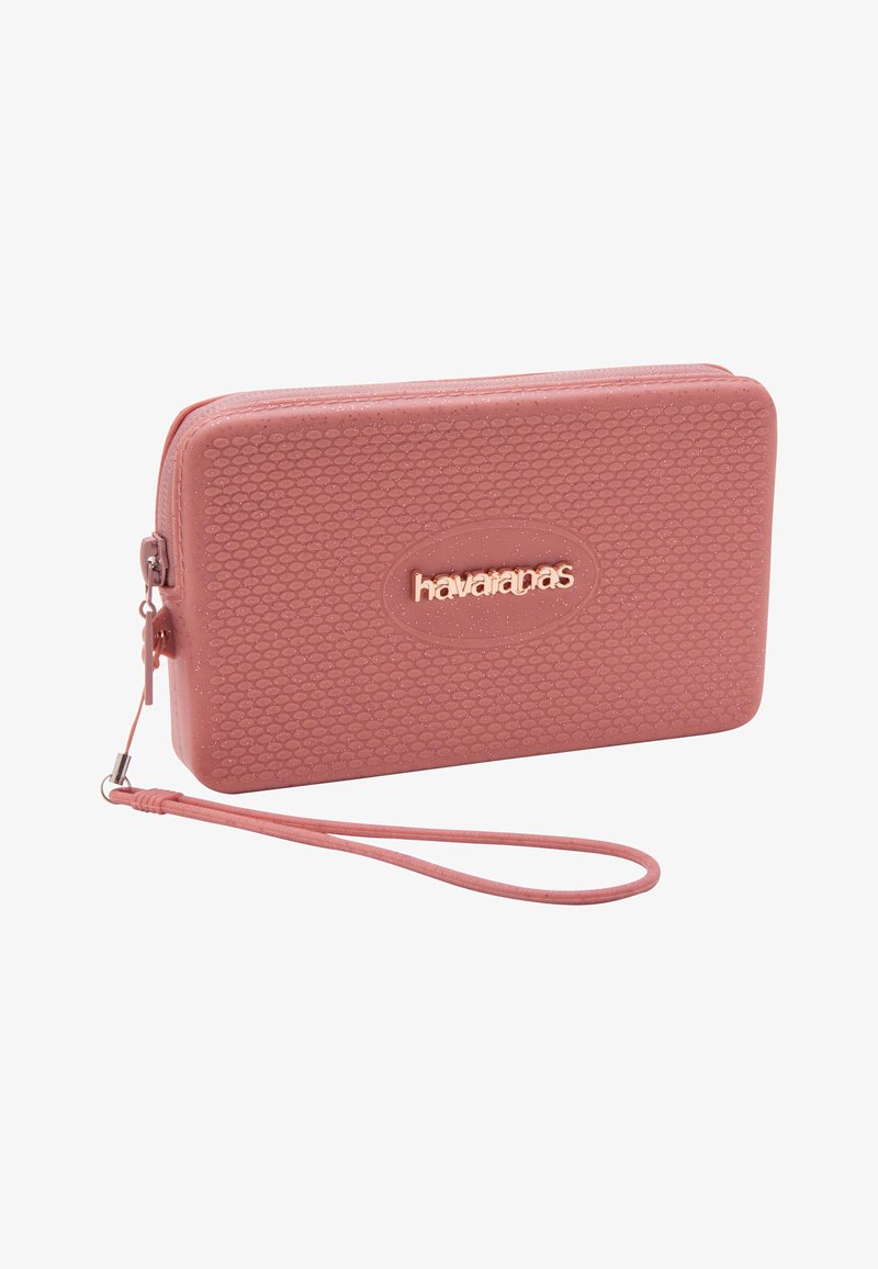 Bolso de mano rectangular rosa con superficie texturizada, cierre de cremallera y logo "havaianas" en letras metálicas en el frente.