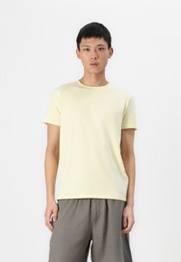 Lichtgele katoenen t-shirt met een ronde hals en korte mouwen, voorzien van een subtiel logo op de linkerkant van de borst, gecombineerd met grijze shorts.