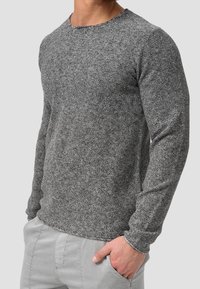 Maglione grigio a maniche lunghe con texture e collo rotondo. Presenta un design aderente e polsini a coste, abbinato a pantaloni grigi chiari.