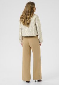 Beige zkrácená bunda s texturovaným vzorem, spárovaná s béžovými kalhotami s vysokým pasem a bočními rozparky. Hladký povrch, elegantní design.