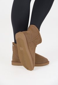 Bruna mocka ankle boots med en texturerad sula och sydda detaljer, bärs med svarta leggings. Sulan har ett vågigt mönster.