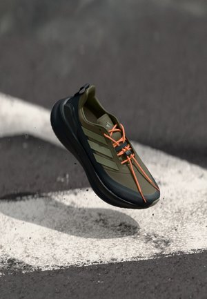 Baskets de sport vert olive avec des accents noirs, des lacets oranges et trois rayures blanches sur le côté. Matière douce et flexible avec une forme arrondie.