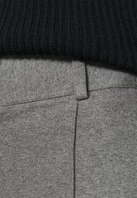 Tejido de punto gris con una textura suave, que presenta una cintura plana y un detalle de costura visible en la parte superior. Un suéter negro acanalado se superpone en la parte superior.