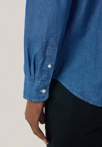 Blauwe spijkerblouse manchetten met knoopsluiting, met een geplooid detail en een ronde zoom. De stof heeft een subtiele textuur.