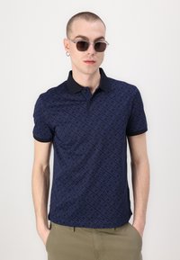 Mørkeblå piké skjorte med teksturert mønster, svart krage, korte ermer og slim fit. Kombinert med klare solbriller.